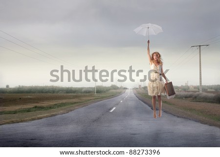 Beautiful woman flying with an umbrella over a countryside road