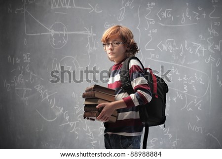 Young student carrying some books with blackboard in the background