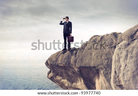 Young businessman using binoculars from a rock over the sea