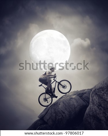 Cyclist climbing a rock under the moonlight
