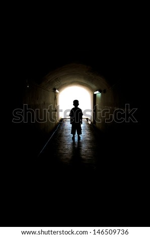 young boy in long tunnel walkway with the white light at the end