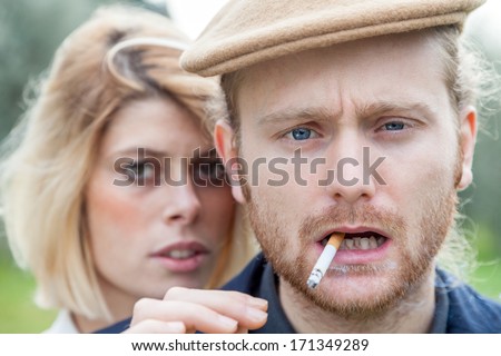 Portrait. Young blond man in a park while he smokes a cigarette in a winter day and to the left a girl with blond hair
