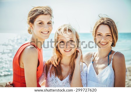 A group of three women friends embrace on the beach in summer. They leave behind the sea and hug looking at camera