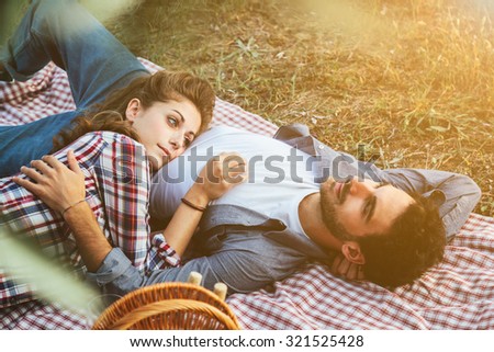 On a late summer day, a pair of young lovers is lying on the grass. The head of the young woman\'s belly on him. Picture taken from the leaves of olive trees in a field the Tuscany, Italy