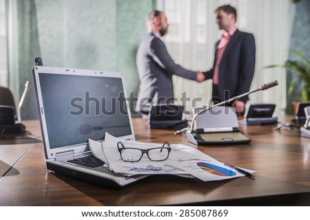 financial chart near dollars seen by unfocused glasses ( colleagues meeting to discuss their future financial plans only silhouettes being viewed ) \
two businessmen shake hands