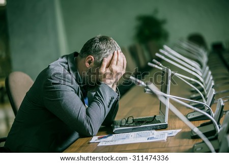 businessman with a big beard in a panic and depression has her head on the backdrop of the conference hall in the green range
