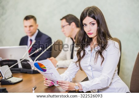close up of a serious  young businesswoman with colleagues in meeting in background at the office