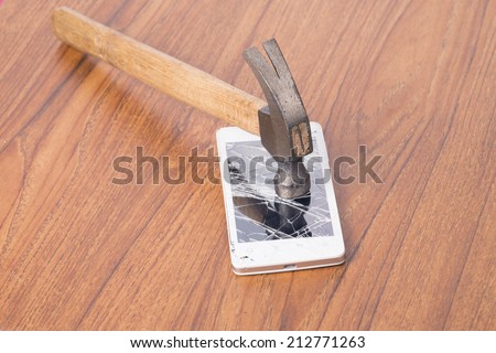 hammer and a smartphone with a broken screen over the wooden surface