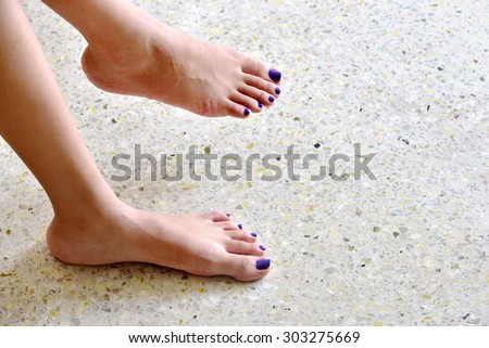 Looking down at the feet of a teenager girl. Dark blue nail polish on the toe nails.