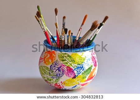 Art work on ceramic pot. Brightly colored Stencil images of leaves on pot painted white. Paint brush holder. Artist\'s workshop.