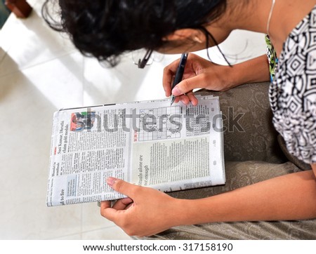 TRIVANDRUM, KERALA, INDIA, SEPTEMBER 12, 2015: Sitting in the porch, teenage girl solving SUDOKU puzzle in the news paper in the morning. view from above. Mental health - concept.