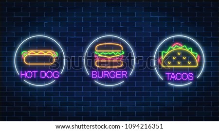 Set of three neon glowing signs of burger, hot dog and tacos in circle frames on a dark brick wall background. Fastfood light billboard symbol. Cafe menu item. Vector illustration.