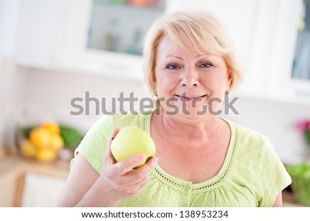 A mature adult woman holding a yellow apple and smiling.