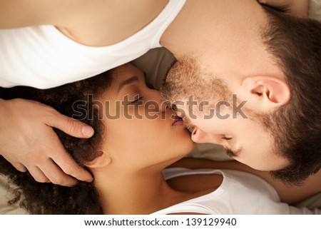 Mixed-race couple kissing in bed.