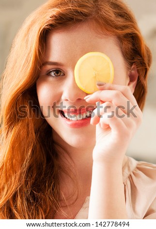 Beautiful smiling red-haired woman holding a slice of lemon in front of her eye