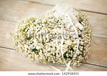 Heart-shaped wedding flower arrangement with wedding rings on it.
