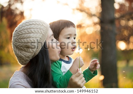 Young mother and her cute son blowing dandelion flowers together.