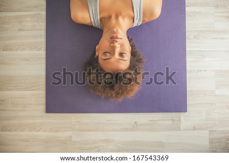 Indoor high-angle shot of an African woman lying on a yoga mat with her eyes closed.