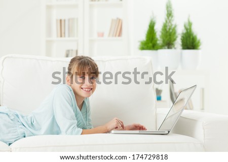 Cute Caucasian girl lying on a sofa and surfing the net at home.