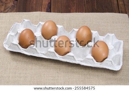 Cardboard egg box with five brown eggs on burlap sackcloth