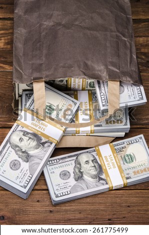 Brown paper bag containing that moolah. Bag full of money - vintage photography of brown paper bag with stacks of hundred dollar bills on wooden background