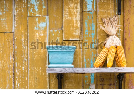 Dry corn cob and vase on wooden rack with yellow wooden wall background grunge style