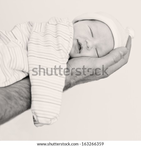 Cute newborn sleeps and smiles at her father\'s hand on a white background (black and white)