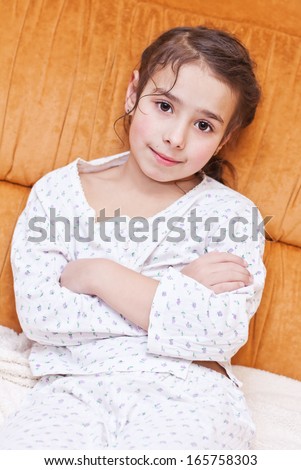 cute little girl in pajamas sitting on the couch on orange background