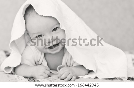 happy baby boy is hiding under the white blanket ( black and white )