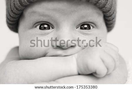 Cute baby boy with wide eyes funny sucks hand closeup ( black-white )