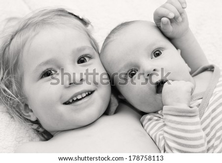 happy little sister hugging her brother lying on a white blanket ( black and white )