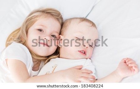 cute little girl hugs a sleeping baby brother on a white background