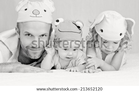 happy dad with kids in funny hats lying on the bed ( black and white )