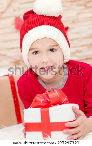 Smiling funny child in Santa red hat holding Christmas gift in hand