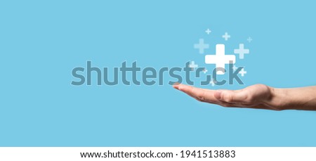 Male hand holding plus icon on blue background. Plus sign virtual means to offer positive thing (like benefits, personal development, social network)Profit,health insurance, growth concepts. Foto stock © 