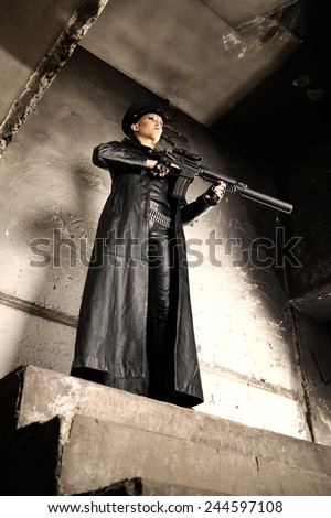 Automatic gun with silencer in hands of woman in leather clothes