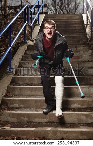 Unhappy and angry man with broken leg in gypsum hardly move on stairs with crutches