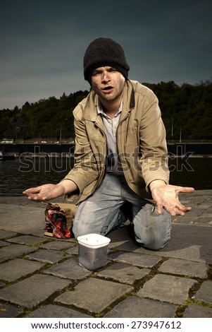 Desperate ugly beggar on river bank
