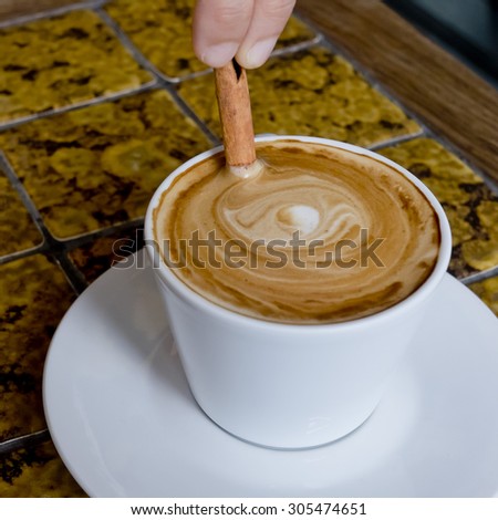 A coffee cup Latte being stirred by Cinnamon sticks.