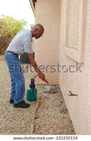 Male senior citizen using a do-it-yourself  pest control kit to spray the side of his house in the backyard.
