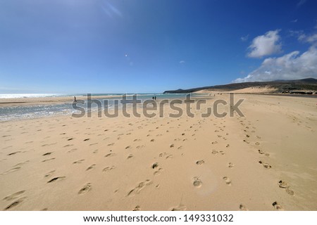 Fuerteventura, Canary islands. Sand beach with footsteps in the sand on a sunny day with a rock in the horizon and a lagoon of water.