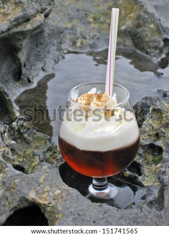 Lanzarote, Canary Islands, Spain. A traditional  Canarian honey-rum (\'ron con miel\') cocktail served with cream and cinamon on top, the glass placed on a volcanic rock.