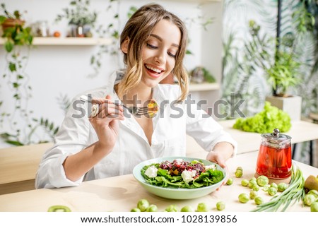 Young woman eating healthy food sitting in the beautiful interior with green flowers on the background ストックフォト © 
