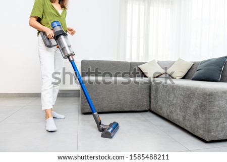 Woman cleaning floor with cordless vacuum cleaner in the modern white living room. Concept of easy cleaning with a wireless vacuum cleaner