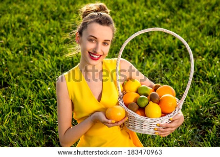 Young woman with basket full of fruits smiling on greenfield of grass in yellow dress
