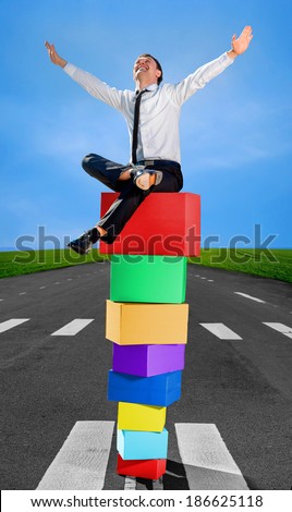 Successful and smiling business man on the top of pyramid made of colorful boxes on the road