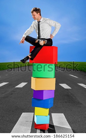 Successful business man on the top of pyramid made of colorful boxes with scorn and pride looks down on the road