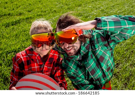 Couple in ski suit and sun glasses have a funny look to the camera on the grass background