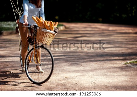 Woman riding the bicycle with the basket full of baguettes on the alley in the park