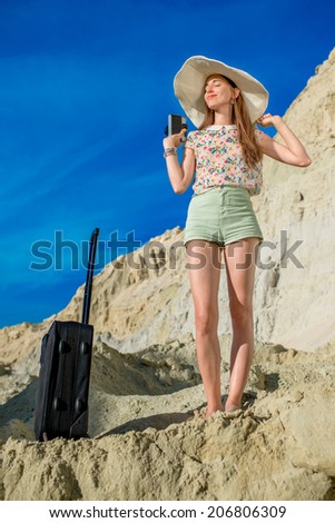 Happy young woman traveler reach the top of sand dunes with baggage and photo camera